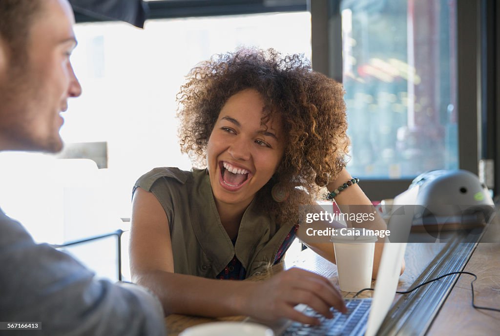 Enthusiastic woman laughing at laptop in cafe