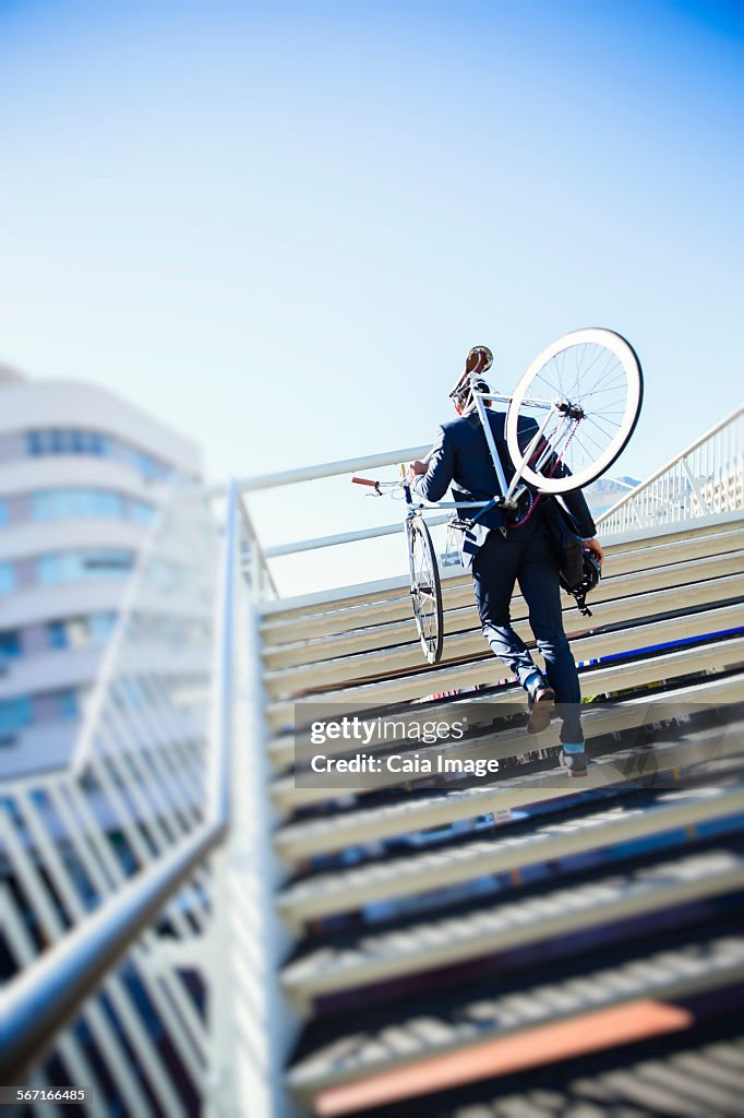 Businessman carrying bicycle up urban stairs under sunny blue sky