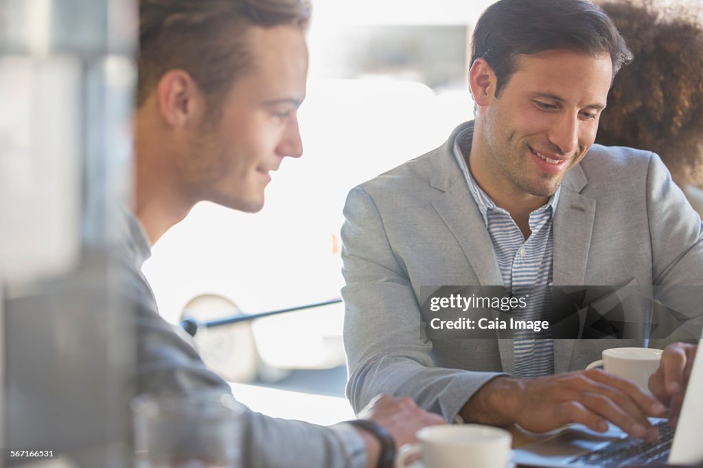 Businessmen with coffee working at laptop in cafe