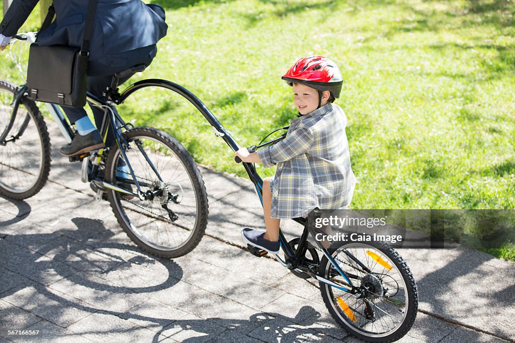 Boy riding tandem bicycle with businessman father in sunny park