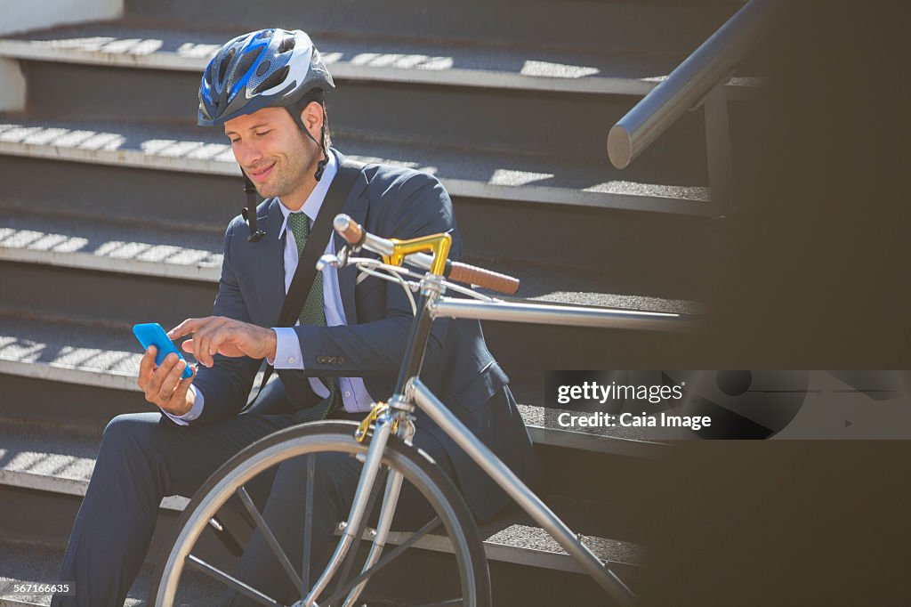 Businessman in suit with bicycle and helmet texting with cell phone on stairs