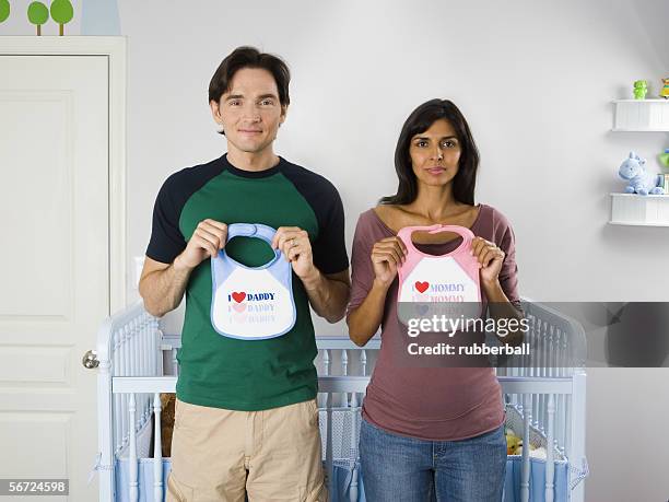 portrait of a couple standing in front of a crib and holding baby bibs - guess jeans stock pictures, royalty-free photos & images