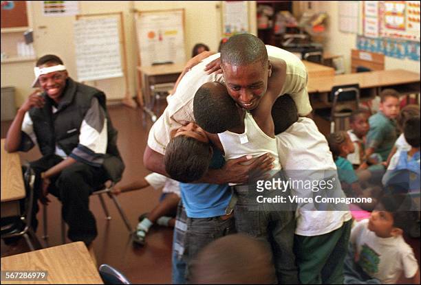 Izaak Chocwe left, rear looks on as Benny Ford gets hugs from youngsters at Grape St Elementary School in Watts, where Ford works at an afterschool...