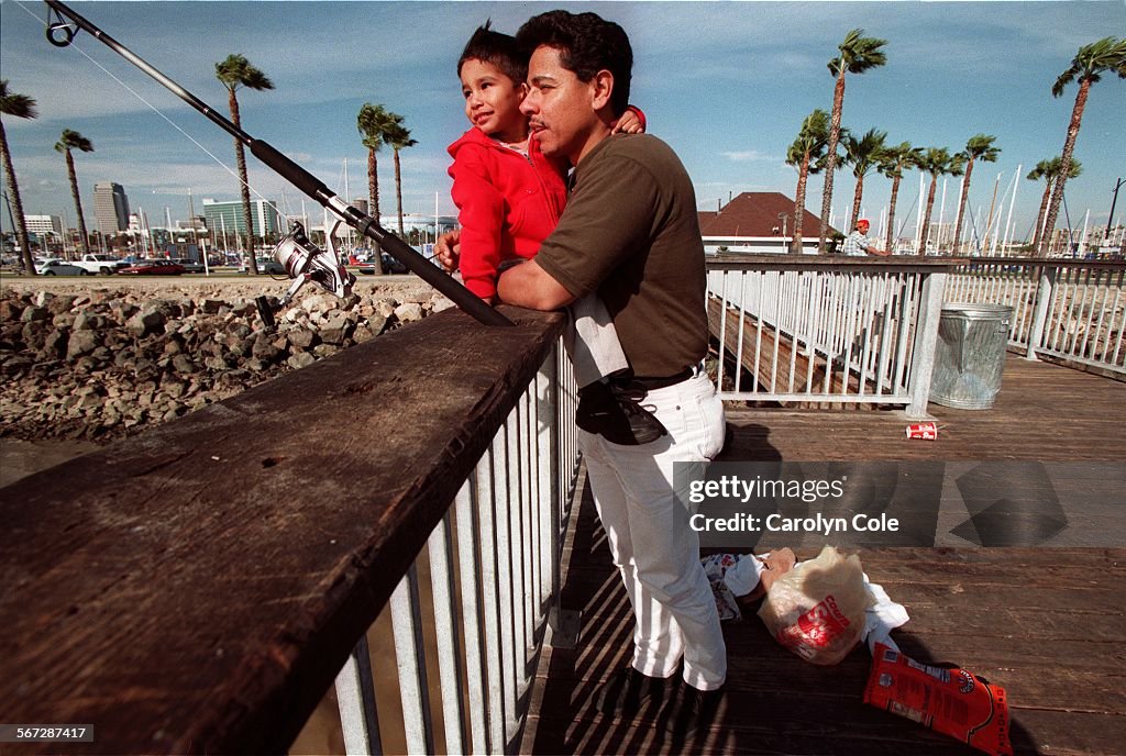 ME.Fishing.0225.CC; Ryan Reyes, age 3, huddles with his father Omar Reyes, against a strong headwind