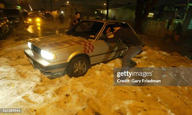 Residents along 110th Street near Compton Ave. Try to push a car stranded in hail after a powerful storm swept thru the area Wednesday night.