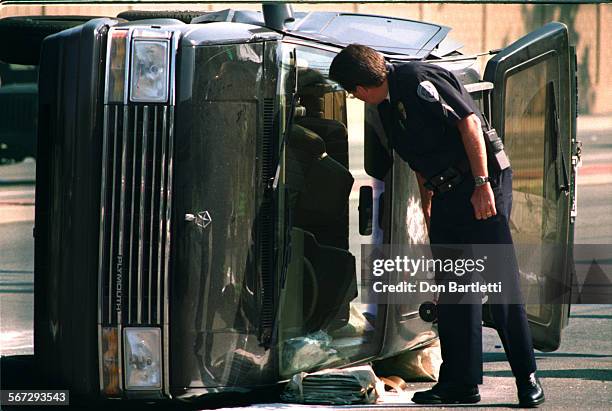 Van.Overturned.DB.3/4/97.FountainValley. A Fountain Valley police officer checks inside an overturned van for any valuables belonging to its driver....
