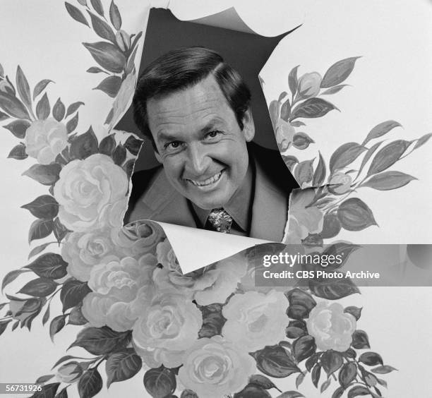 American game show host Bob Barker thrusts his head out of a hole in rose-patterned paper for a publicity photo promoting the Tournament of Roses...