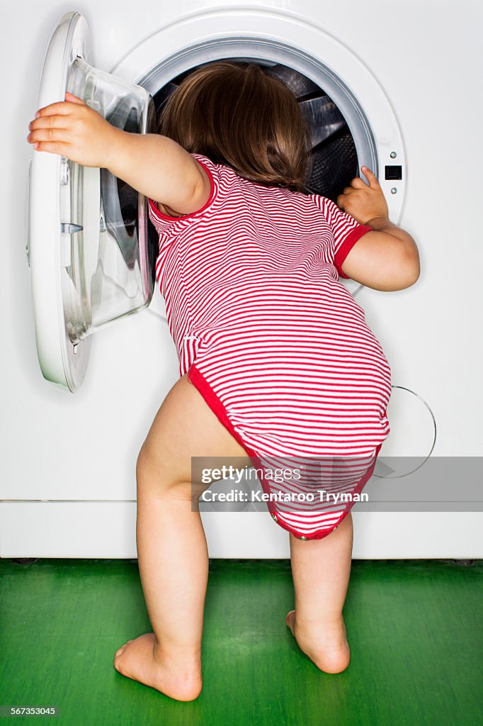 Rear view of baby girl peeking into washing machine at home