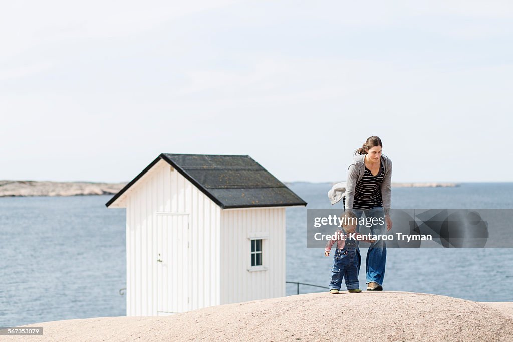 Mother and baby girl walking at beach by beach cabin against clear sky