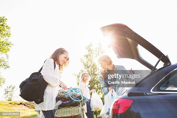 male and female friends unloading car on field against clear sky - 3 guy friends road trip photos et images de collection