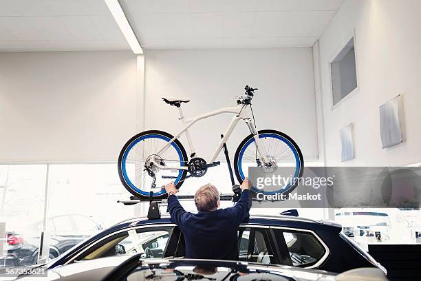 rear view of senior man adjusting bicycle on car roof at showroom - exercise machine stock pictures, royalty-free photos & images
