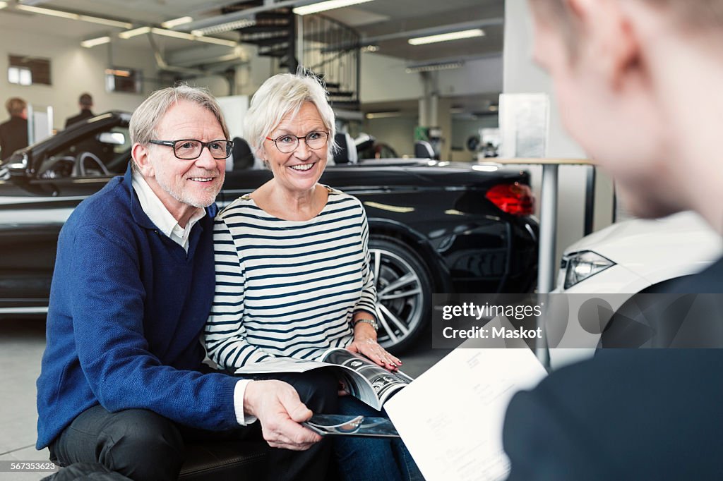 Happy senior couple looking at salesman in car showroom