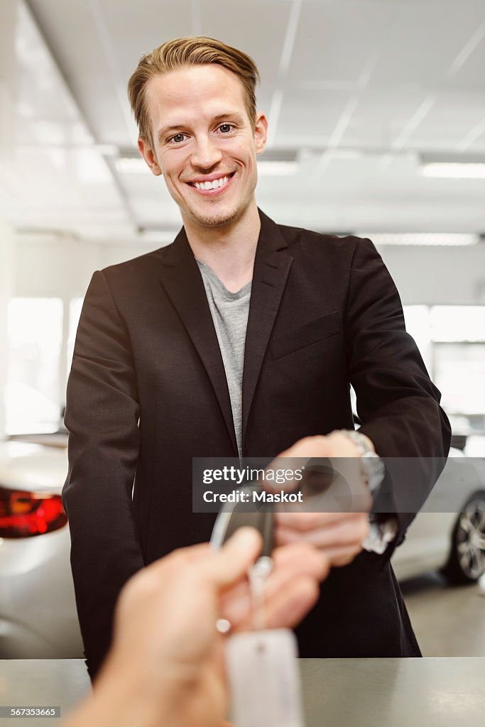 Portrait of happy man receiving keys from saleswoman in car dealership