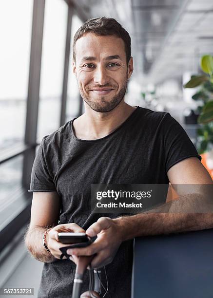 portrait of smiling businessman holding mobile phone while leaning on cubicle in office - 30 34 jaar stockfoto's en -beelden