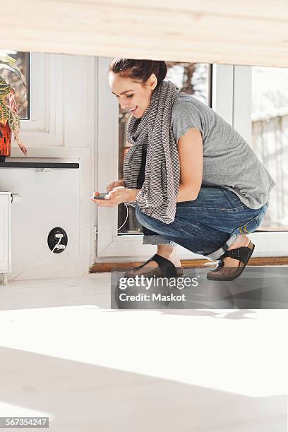 side view of woman connecting mobile phone to charger at home - enchufar fotografías e imágenes de stock
