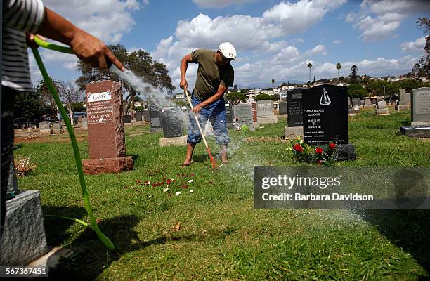Ana Paz waters while her husband Rayne Climaco cuts the grass in and around her Grandmother's grave at the Evergreen Cemetery in Boyle Heights Sept....