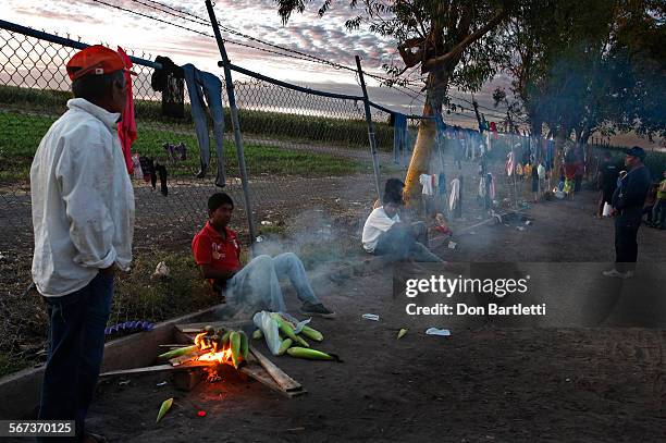 As the day draws to a close, a resident of Campo Isabeles roasts corn scavenged from the field in the background. Everyone in the camp works for Rene...