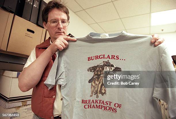 CopDogs.#2.0223.BC/dAttorney Donald Cook holds up police tshirt featuring a police dog holding a severed limb and the inscription, "Burglars;...