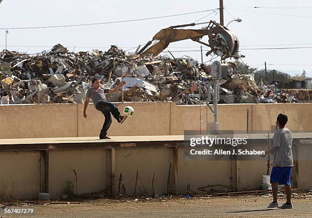 With airplanes taking off overhead, heavy machinery piles up a large stack of metal at the Main St. Recycling Yard while Abraham Solis left, and...