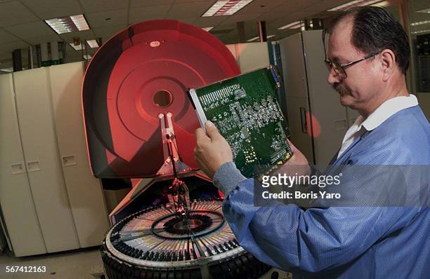 Teradyne employe Carlos Ruiz examines a PC board from the test bine of the J973 which the company makes to inspects semiconductors and other...
