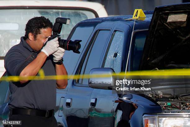 Crime scene investigator from Los Angeles County sheriff photographs bullet holed window of a black SUV in which a fatal gunshot victim was located...