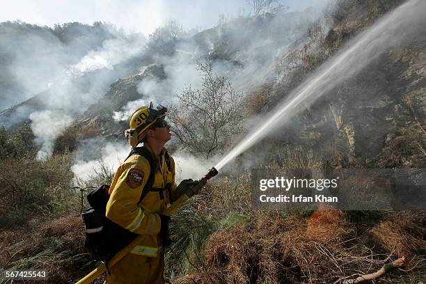 Cal Fire firefighter Jeff Newby, Engine 3480 shoots water on smoldering brush on a hillside along Highway 39 in Azusa. The Colby fire that has been...