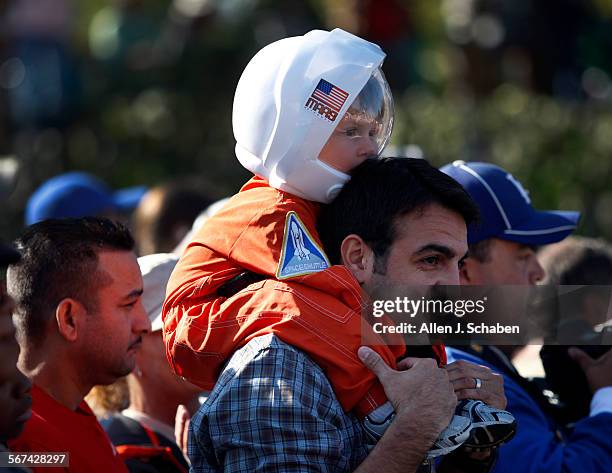 Clark Ferrer of La Mirada, top, peers out of his space helmet, while sitting on his father, Juan Ferrer's shoulders as they watch the Space shuttle...