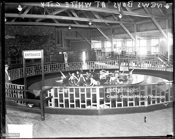 Informal full-length portrait of Daily News boys lying on a large circular floor and waving, part of a ride at the White City amusement park,...