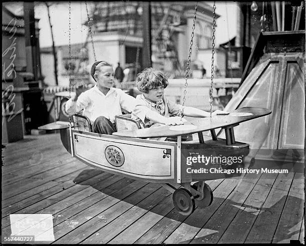 Full-length portrait of a girl and boy sitting in a small airplane on a ride at the White City amusement park, located at 63rd and South Parkway in...