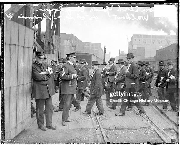 Image of packinghouse workers during their walkout, crossing train yards, Chicago, Illinois, 1919. Police officers are standing by watching.