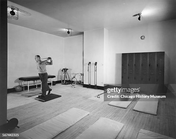 Interior view of an exercise room, showing a man practicing his golf swing amid various kinds of fitness equipment, at the Field Building , Chicago,...