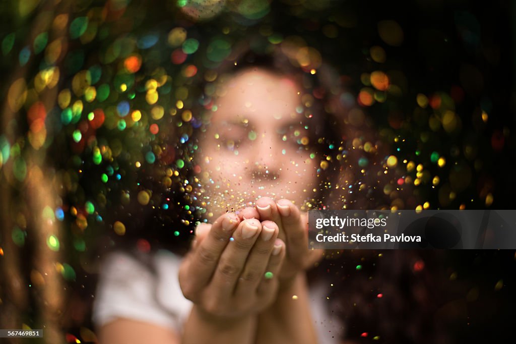 Young woman blows glitter into the air