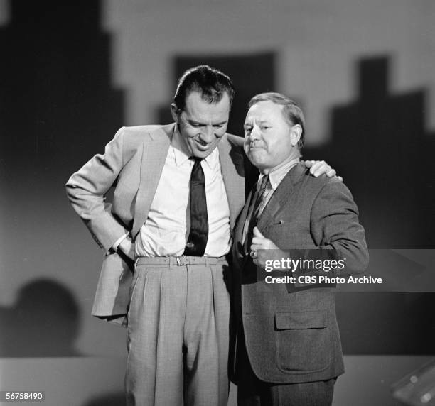 American television personality Ed Sullivan stands with his head down and arm over the shoulder of American actor Mickey Rooney on an episode of...