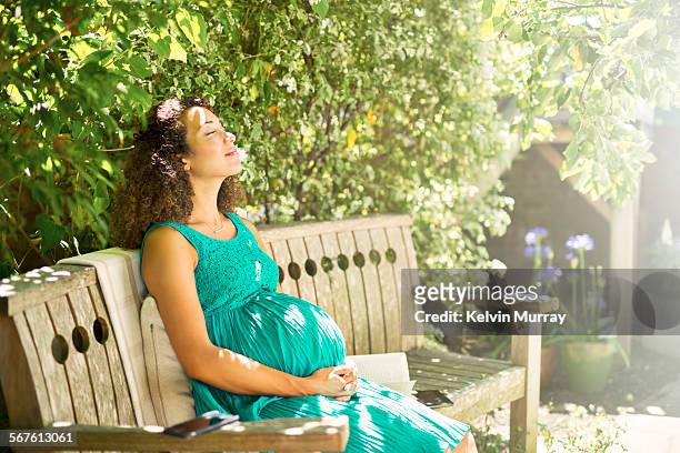 a mixed race pregnant lady relaxes in sunny garden - prenatal care ストックフォトと画像