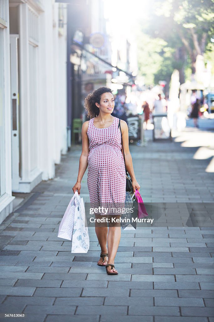 Pregnant mixed race lady walks with shopping