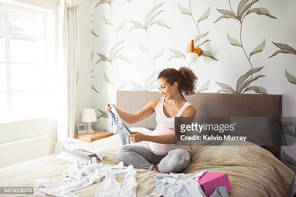 a pregnant lady looks through baby clothes - baby clothing stock pictures, royalty-free photos & images