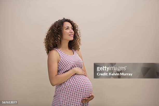a pregnant mixed race lady holds bump thoughtfully - mujer embarazada fotografías e imágenes de stock