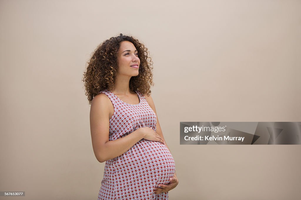 A pregnant mixed race lady holds bump thoughtfully