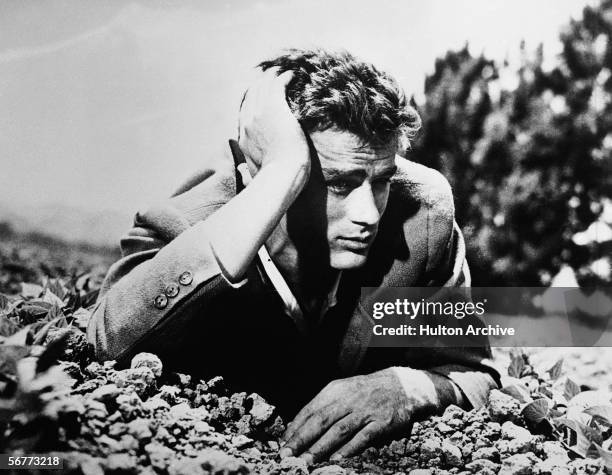 American actor James Dean lies in the dirt with his head leaning on his hand, 1950s.