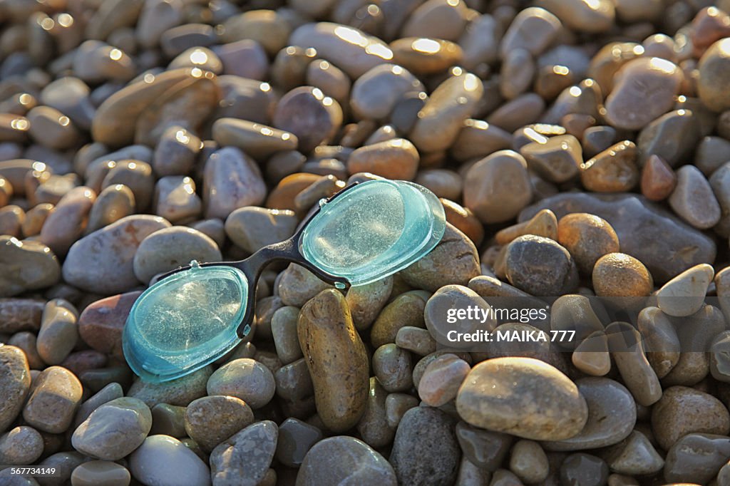 Trash washed swimming goggles on beach of stones