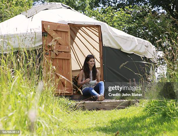 woman sitting in yurt doorway eating cereal - rundzelt stock-fotos und bilder