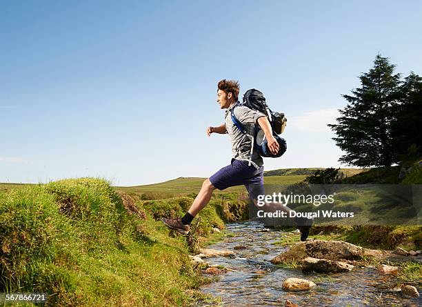 hiker stepping over stream in countryside. - running man profile stock pictures, royalty-free photos & images