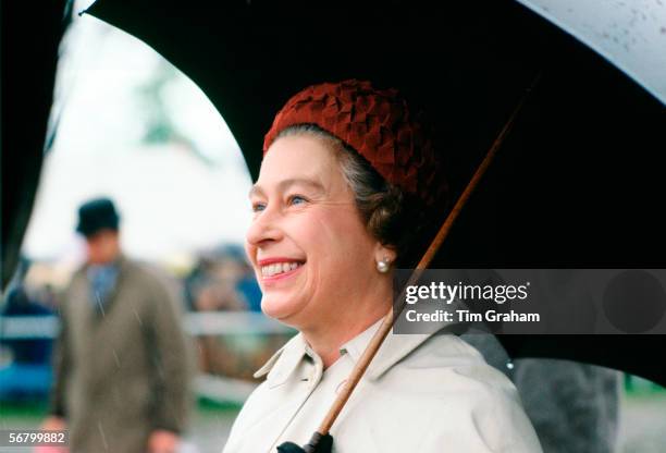 Queen Elizabeth II taking shelter under an umbrella whilst presenting prizes at the Royal Windsor Horse Show.