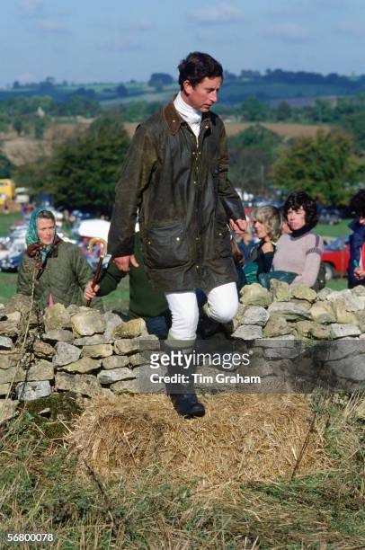 Prince Charles dressed in a Barbour jacket and wellington boots steps over a stone wall whilst watched by Lady Sarah Keswick and Camilla...