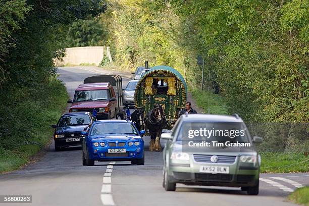 Cars overtake shire horse-drawn gypsy caravan on country lanes, Stow-On-The-Wold, Gloucestershire, United Kingdom.