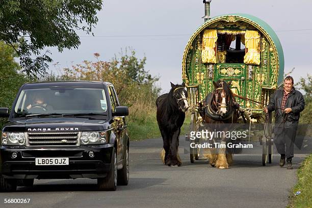 Range Rover car overtakes shire horse-drawn gypsy caravan on country lane, Stow-On-The-Wold, Gloucestershire, United Kingdom.
