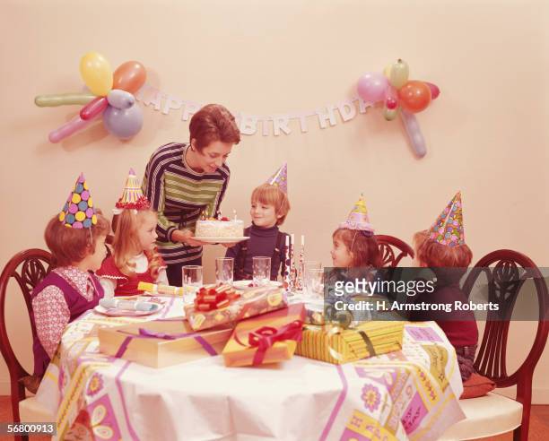 1970s: Five children at birthday party, mother serving birthday cake.