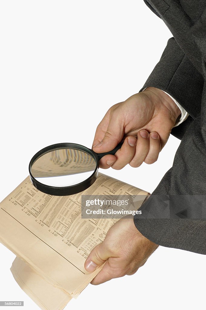 Close-up of a businessman holding a magnifying glass over a newspaper