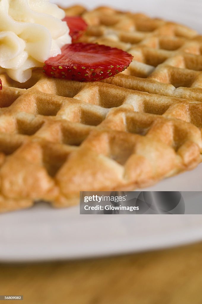 Close-up of a waffle with whipped cream and strawberry slice on it