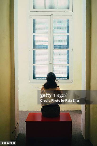 woman sitting on bench in front of closed window - woman prison stock pictures, royalty-free photos & images